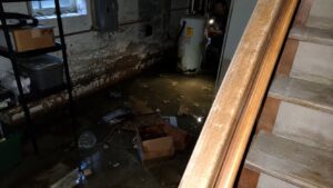 Submersible pump extracting standing water from flooded residential basement with professional restoration crew