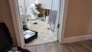 Technician in full PPE performing substrate treatment during toilet overflow Category 3 cleanup with containment